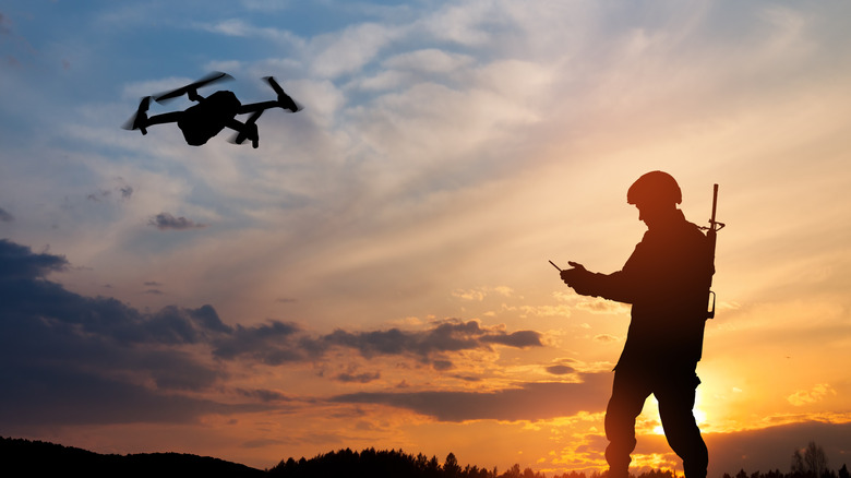 Soldier controlling a drone, silhouetted against setting sun.