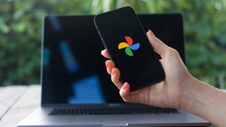 Mano sosteniendo un teléfono con el logotipo de Google Photos frente a la computadora portátil