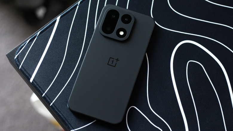 Black OnePlus 15 on a black and white deskmat