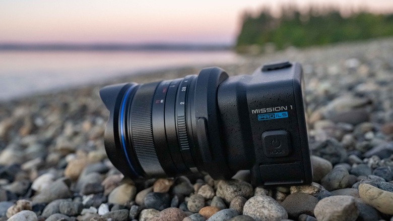 The GoPro Mission 1 Pro ILS with the Laowa 7.5mm f2.0 lens resting on a gravel beach by the sea.