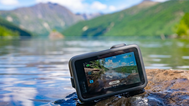 The GoPro Mission 1 Pro by the edge of a mountain lake, with the lake seen on the screen in timelapse mode.