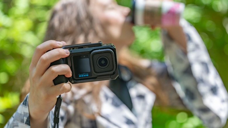 A woman holding the GoPro Mission 1 Pro in its point and shoot case while drinking coffee.
