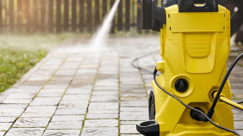 Yellow pressure washer on a pavement while it's being sprayed in the background