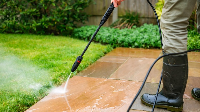 Man in black boots cleaning patio with a black pressure washer