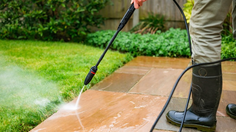 Man in black boots cleaning patio with a black pressure washer