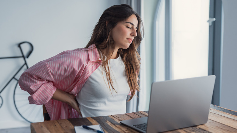 A woman at a desk, struggling with back pain