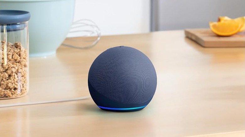 An Amazon Echo Dot on a table with granola and oranges.