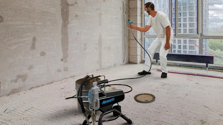 A man wearing mask using Avanti paint sprayer over a wall