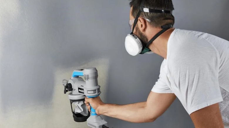 A man using blue and grey color Avanti paint sprayer over a wall