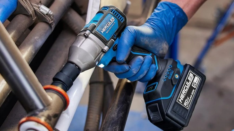 A worker wearing blue gloves using a Hercules impact wrench