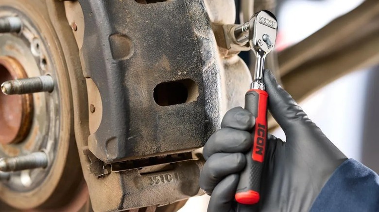 Close-up of a gloved hand using an Icon G2 ratchet on a car's brakes