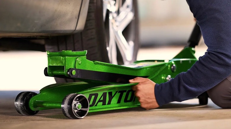 A person sliding glittery green Dayton jack under a car