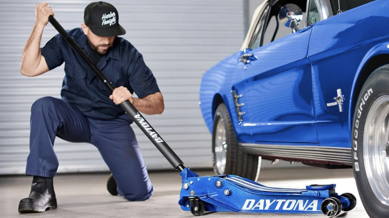 A man using the Daytona Superduty Floor Jack on a matching blue car