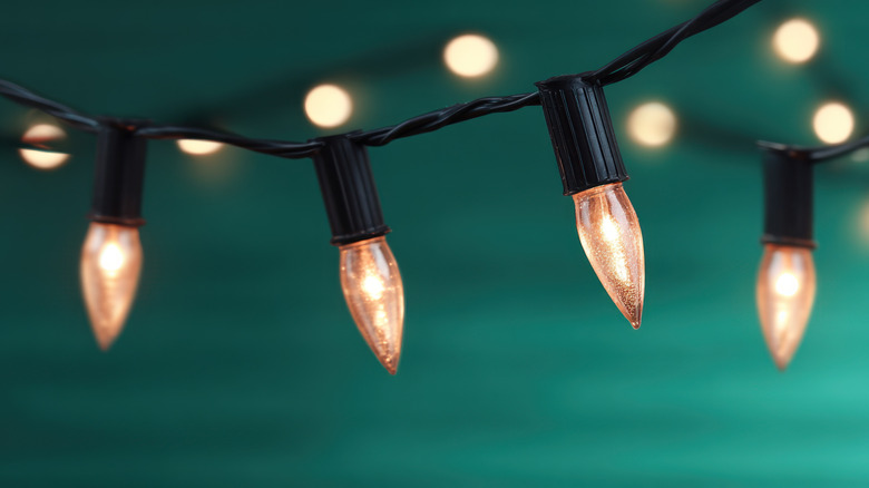 A close-up of four string lights emitting a warm light against a blurred teal background.