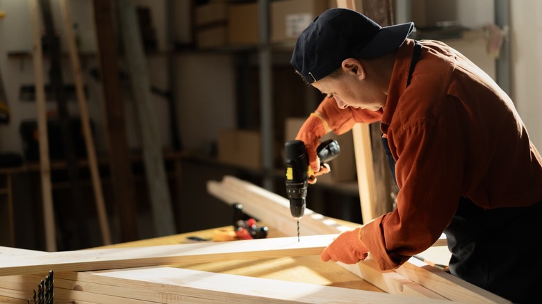 Carpenter drilling hole into timber block