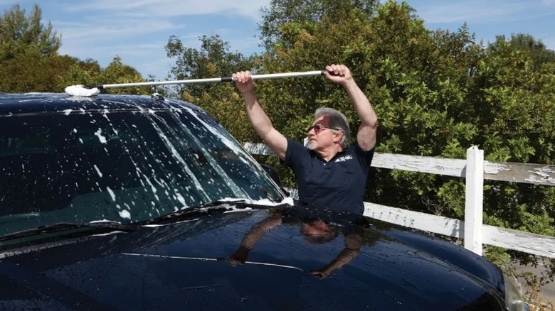 Man washing the top of a black vehicle with a long-handled tool