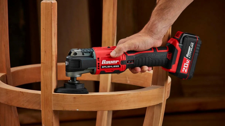 Person using a Bauer multi-tool to sand the underside of a round wooden stool