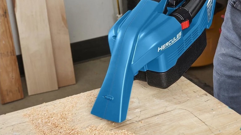 A person using a Hercules shop-vac to remove sawdust from a work surface.