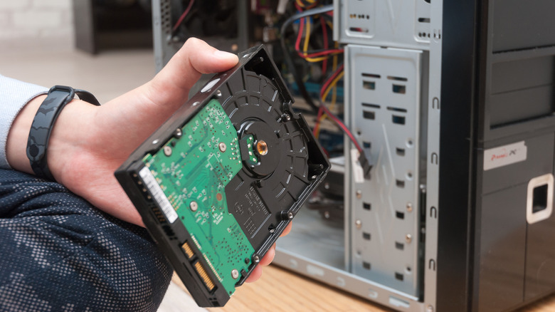 A person showing a hard drive near a CPU