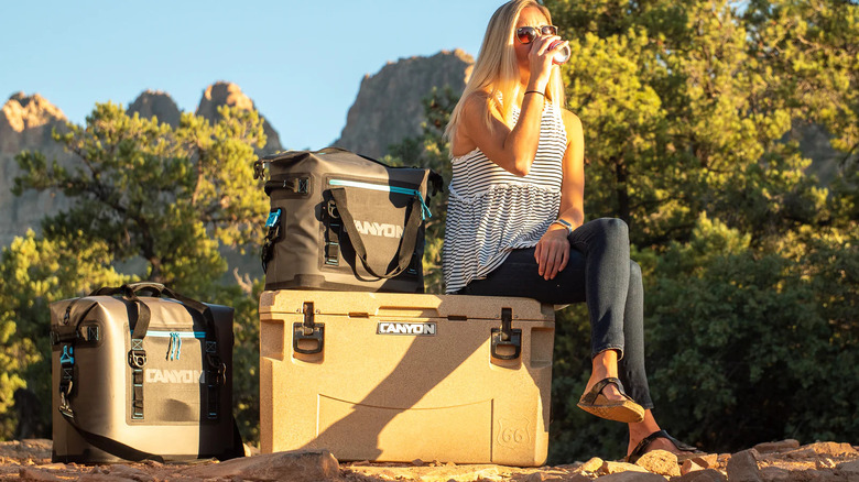 A woman sitting on a Canyon hard cooler, with two Canyon soft coolers to her side