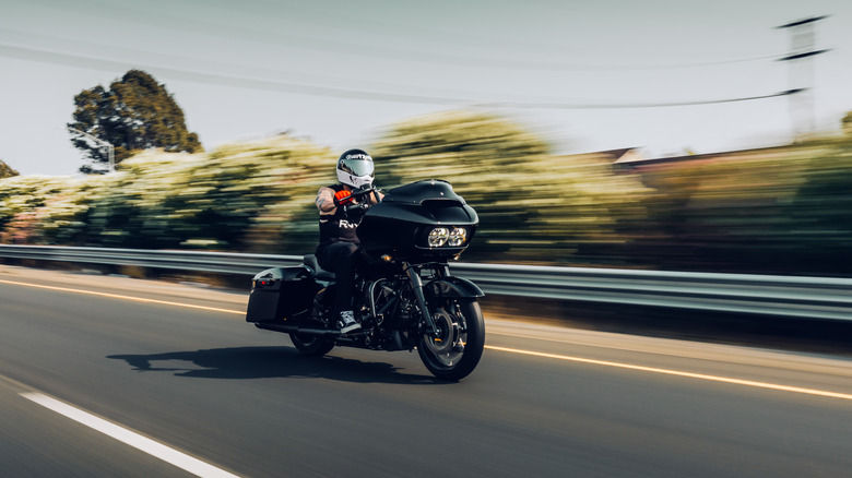 A man drives a black Harley-Davidson tourer at speed down a road