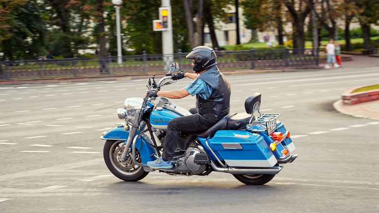 A biker riding blue Harley Davidson Road King while turning onto a road