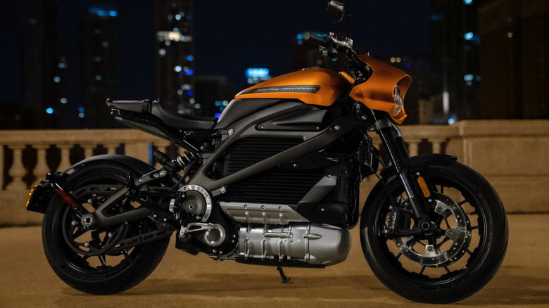 An orange and black Harley livewire standing against a city backdrop at night