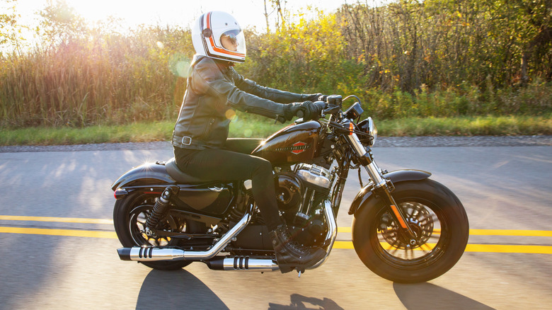 A helmeted rider cruising down a forested road on a 2021 Harley Sportster Forty Eight