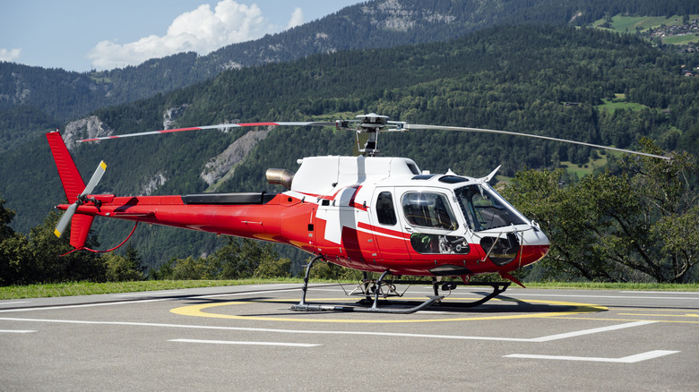 Red and white helicopter landed on a mountain helipad with the Alps in the background