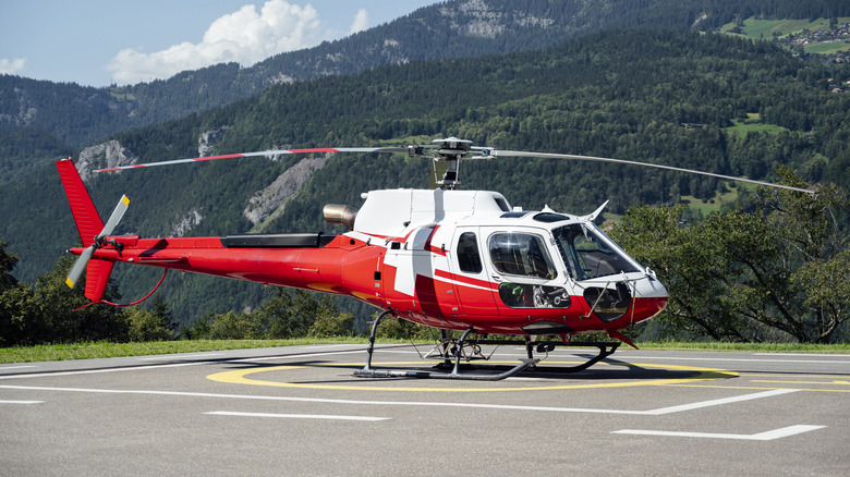 Red and white helicopter landed on a mountain helipad with the Alps in the background