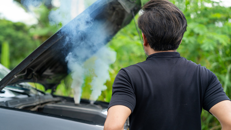 Man standing next to a car with underhood smoke