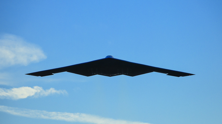A B-2 Spirit flying against a blue sky with clouds