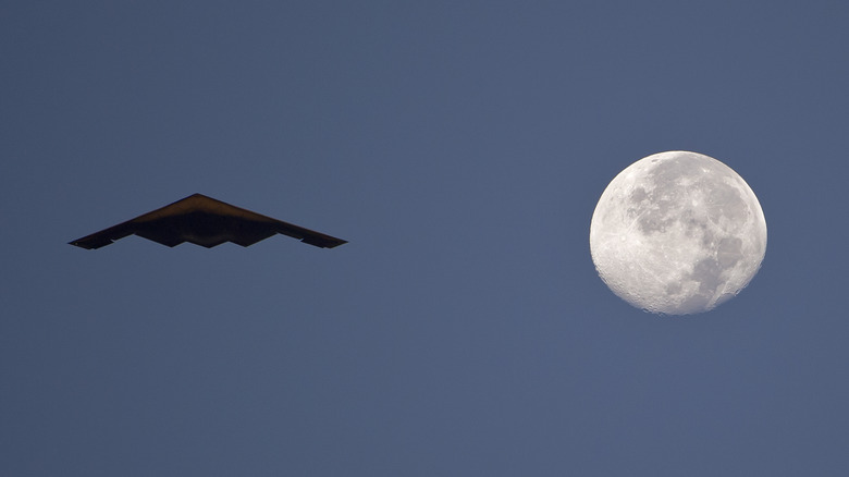 A B-2 Bomber flying next to a full moon in the night sky