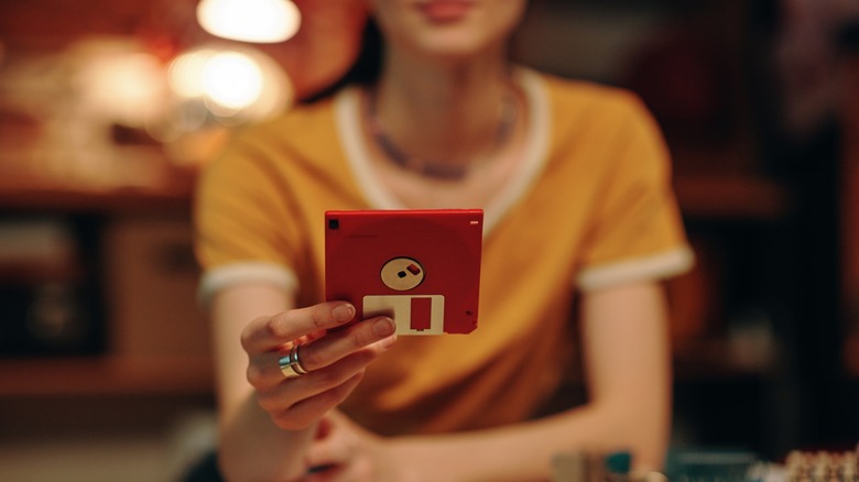 Person offering a red floppy disk