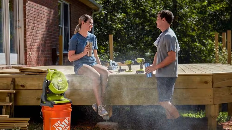Man and woman talking on deck with Ryobi bucket top misting fan powered on