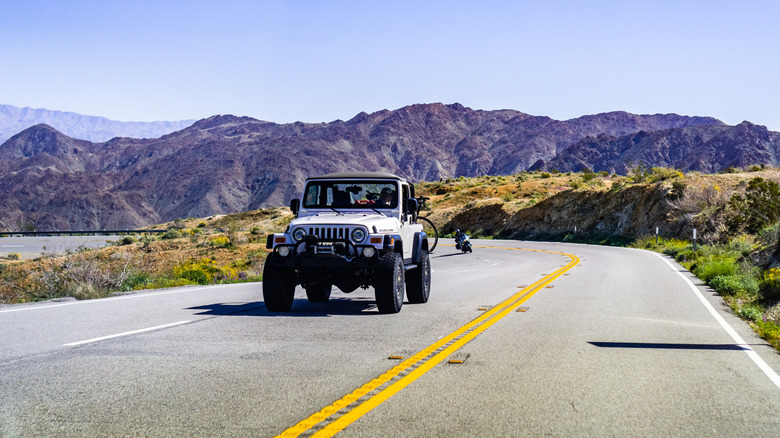 A white jeep driving on a highway road with a mountain in the background