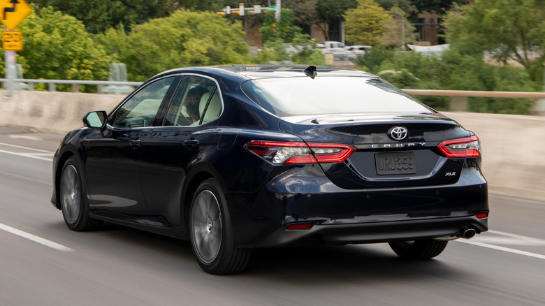 Rear 3/4 view of blue 2021 Toyota Camry driving on highway.