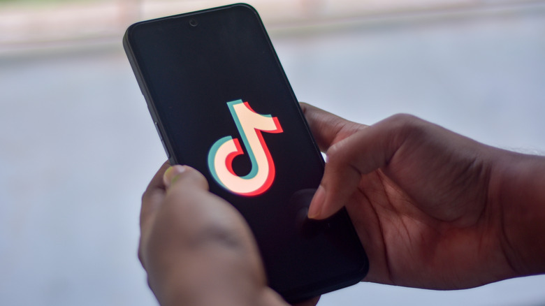 A smartphone held in two hands. The screen is showing the TikTok logo.