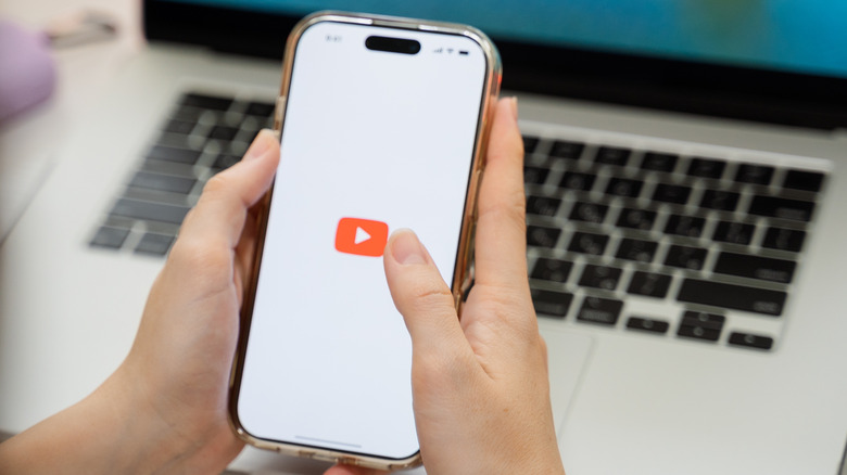 A smartphone being used over a MacBook with the YouTube loading icon.