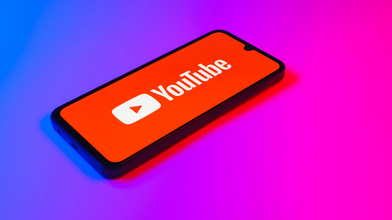 A smartphone with the YouTube logo on it on a gradient background.