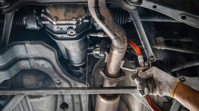 Mechanic filling rear differential fluid in car on lift