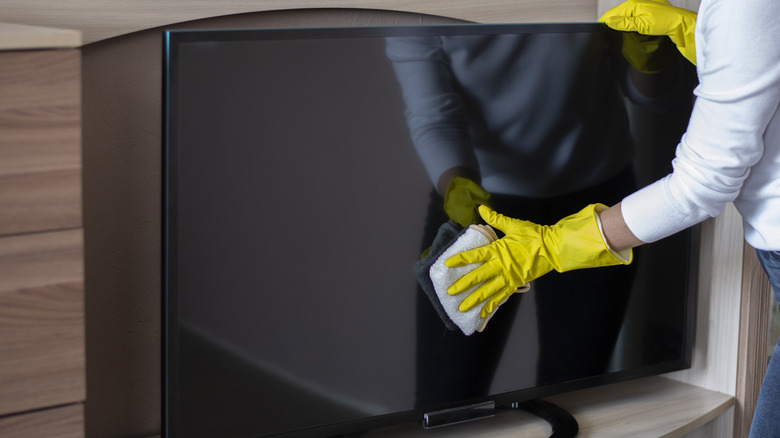 person wiping tv screen with gloves