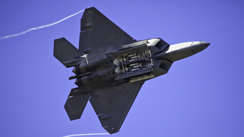 Un Raptor F-22 en el aire contra un cielo azul, con muelles de misiles abiertos