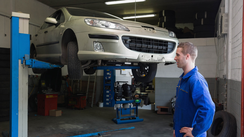 A mechanic standing in front of a two-post car lift holding a car in a workshop.