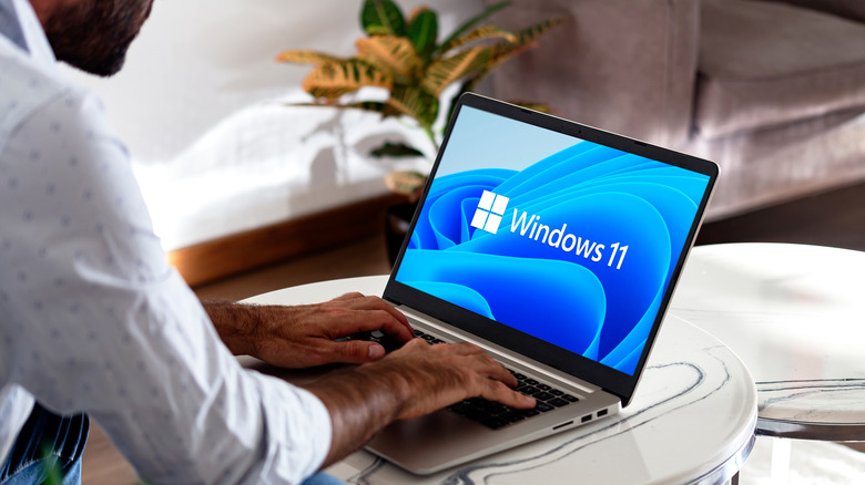 A man using a laptop that's displaying the Windows 11 logo on the screen.