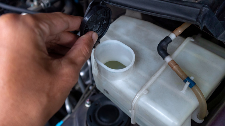 A hand holding the cap to a windshield wiper fluid reservoir.