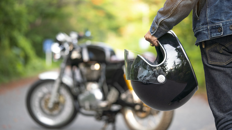 Person holding a helmet and walking toward a motorcycle