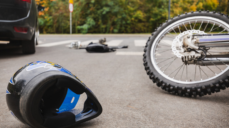 Motorcycle helmet on the ground next to a motorcycle wheel and parked car