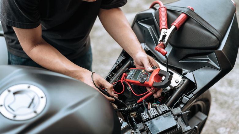 A person inspects a motorcycle battery on the side of the road