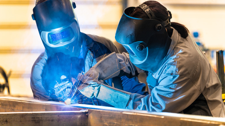 Two welders wearing helmets and working together on welding project.